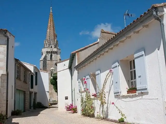 Ruelle aux maisons blanches et volets bleus à Sainte-Marie-de-Ré, clocher en arrière-plan
