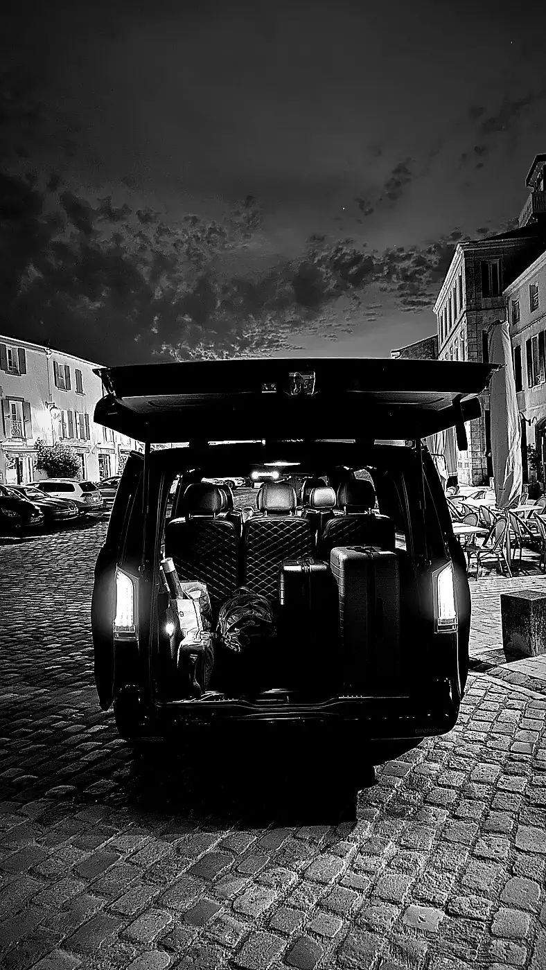 Van MyCourse de nuit, coffre ouvert sur une place pavée, en noir et blanc