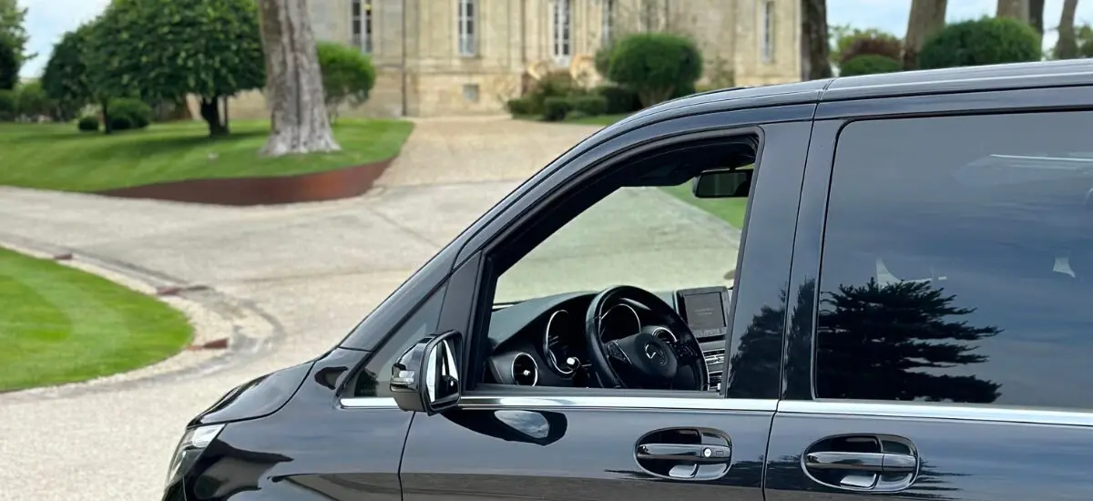 Black vehicle parked on driveway, scenic garden, historic-style building in background.