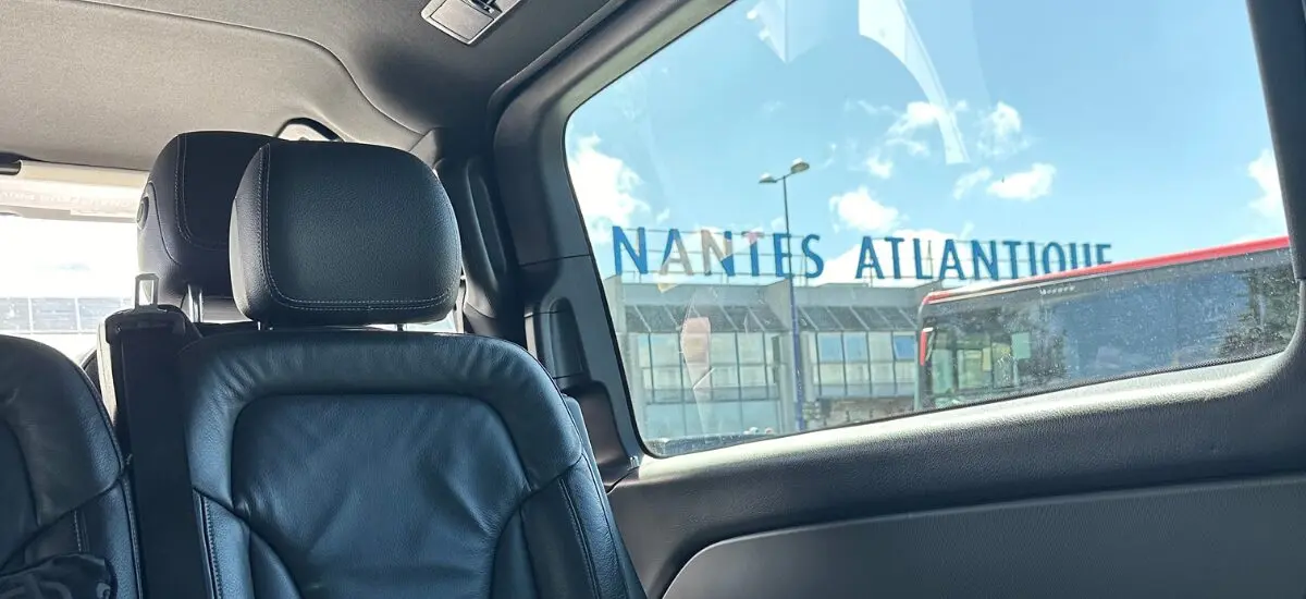 Vehicle interior with black leather seats, view of Nantes Atlantique Airport through window.