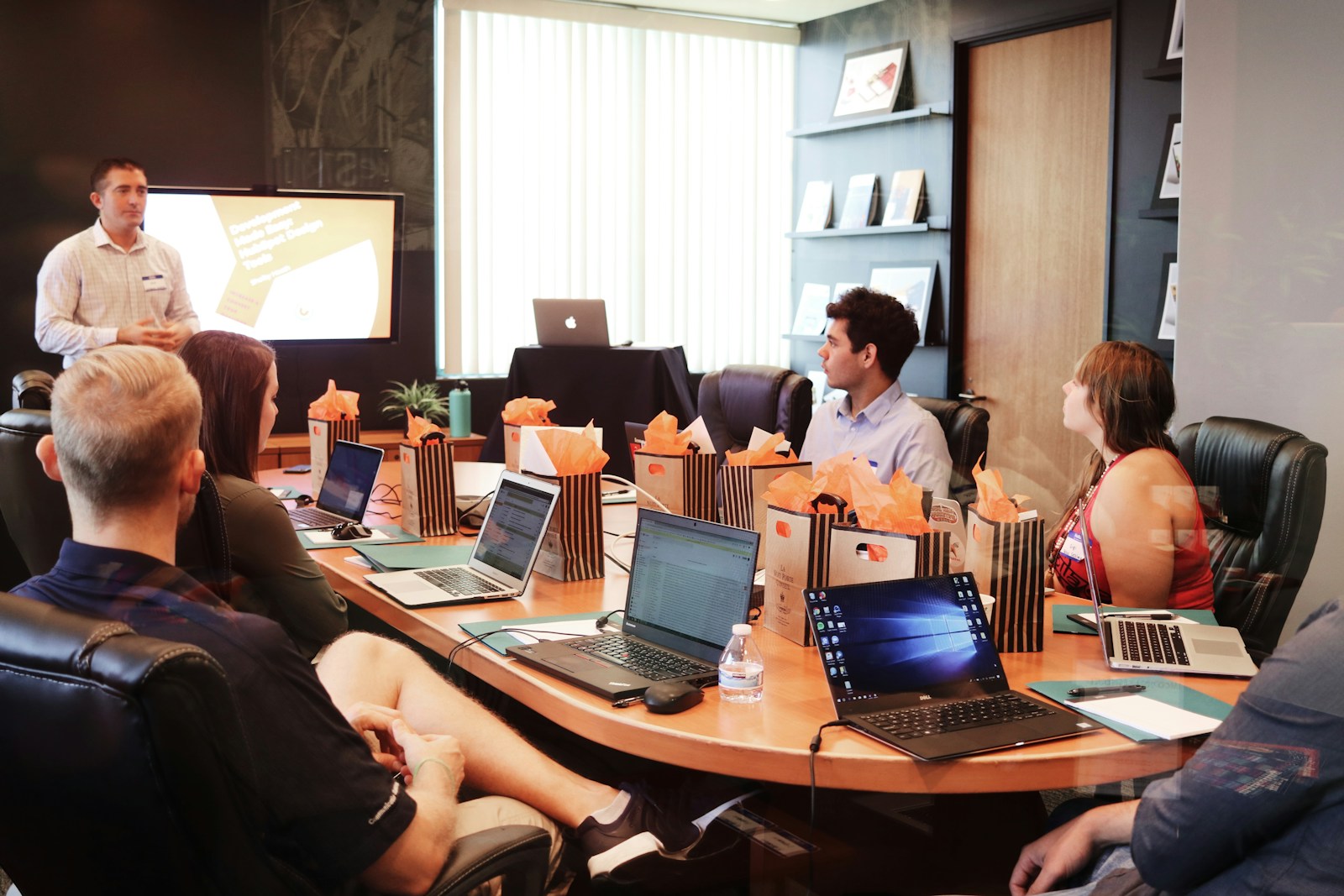 People in a conference room watching a presentation with laptops and gift bags on the table.